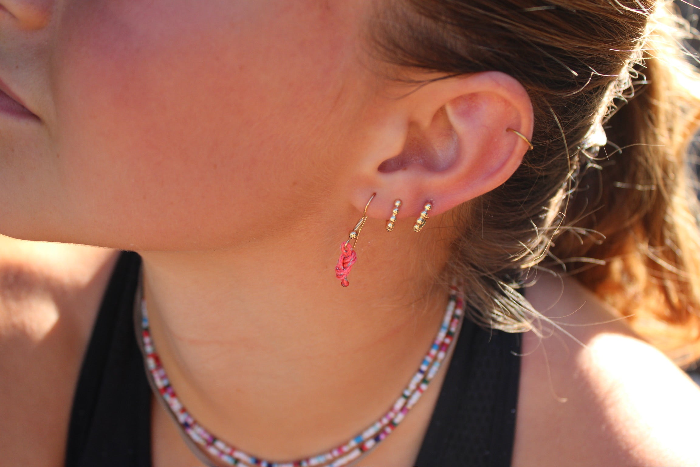 Pink figure eight earrings with reflectors and gold hooks, worn