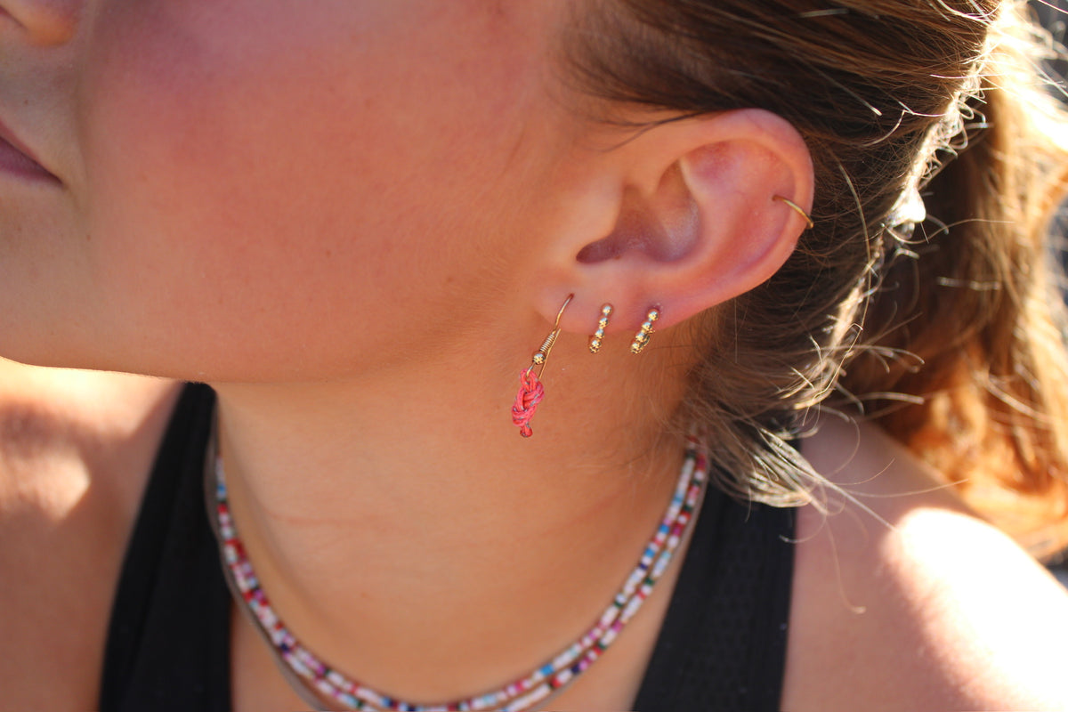 Pink figure eight earrings with reflectors and gold hooks, worn